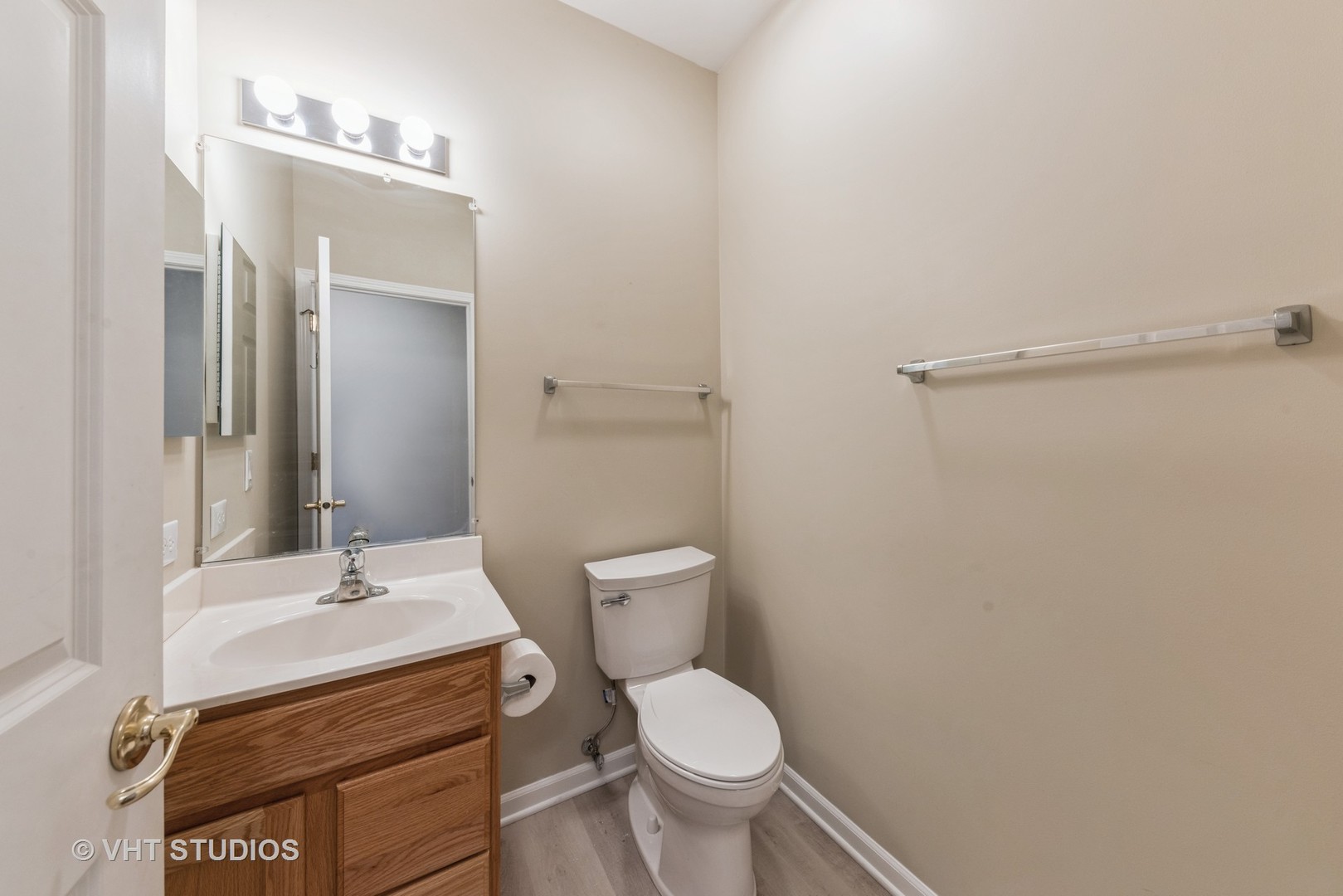Bathroom with a wood vanity, large mirror, toilet, and wall-mounted towel bars.