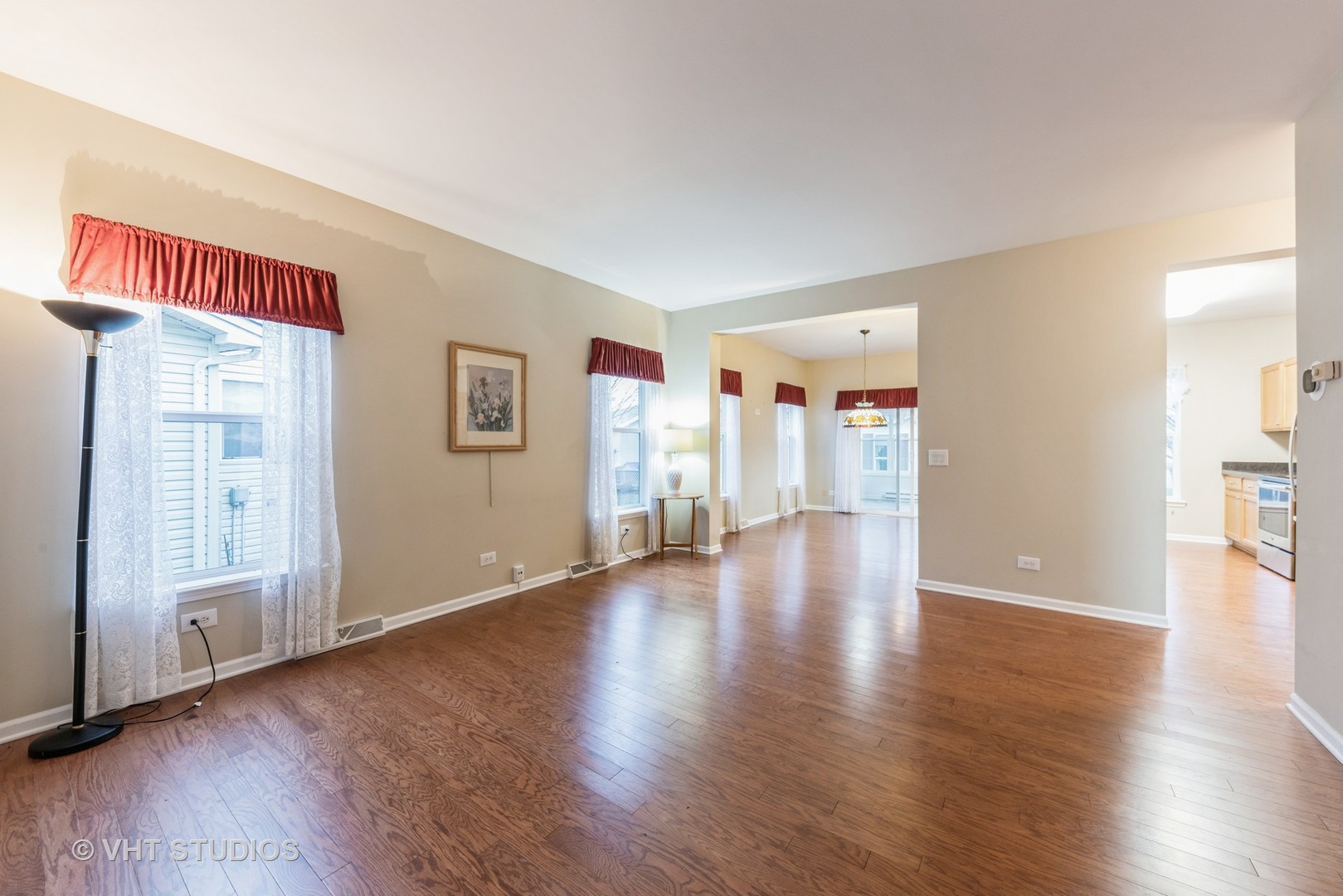 Living room with hardwood floors, tall curtained windows, and openings to the dining area and kitchen.