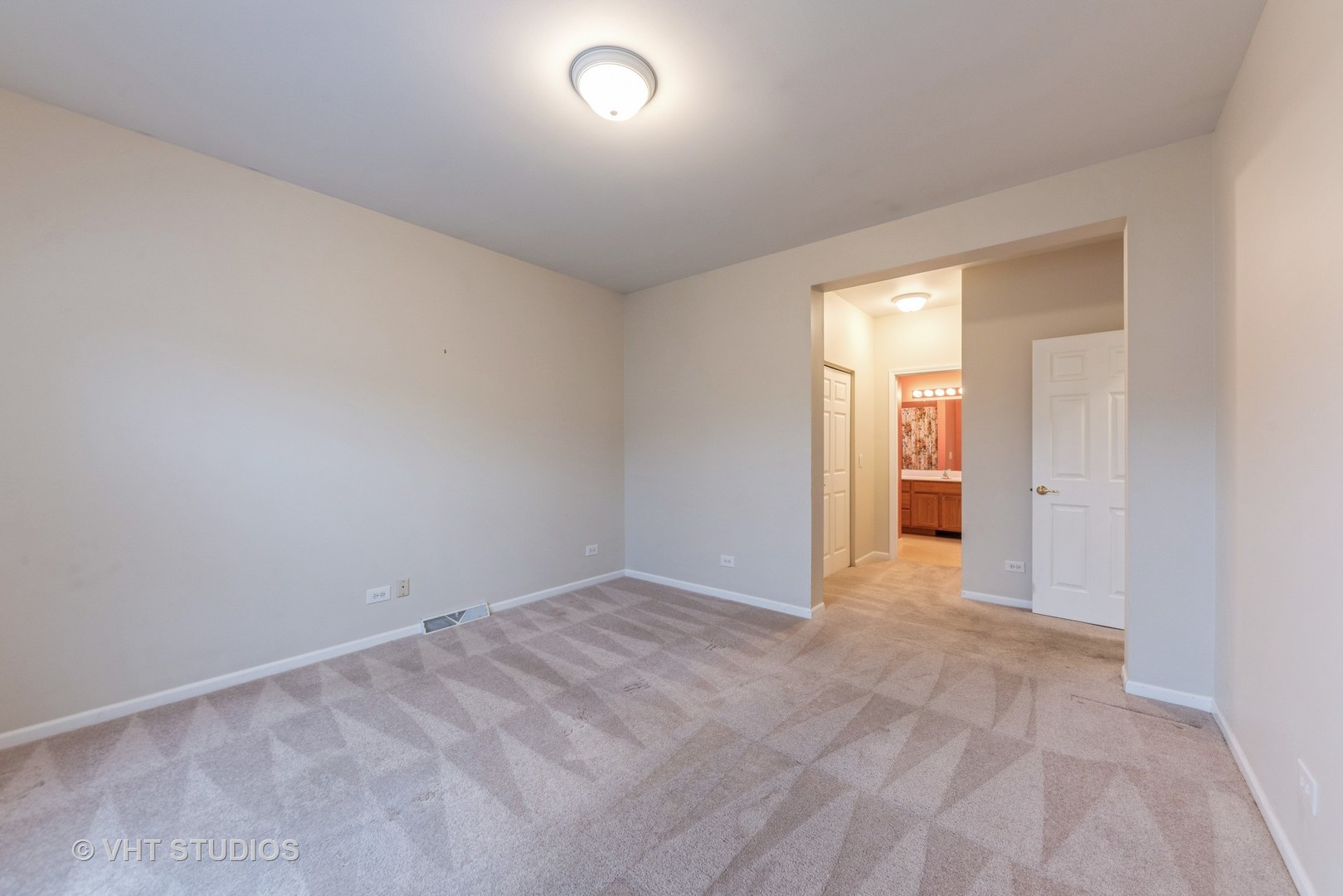 Empty carpeted bedroom with an open doorway to a bathroom vanity.