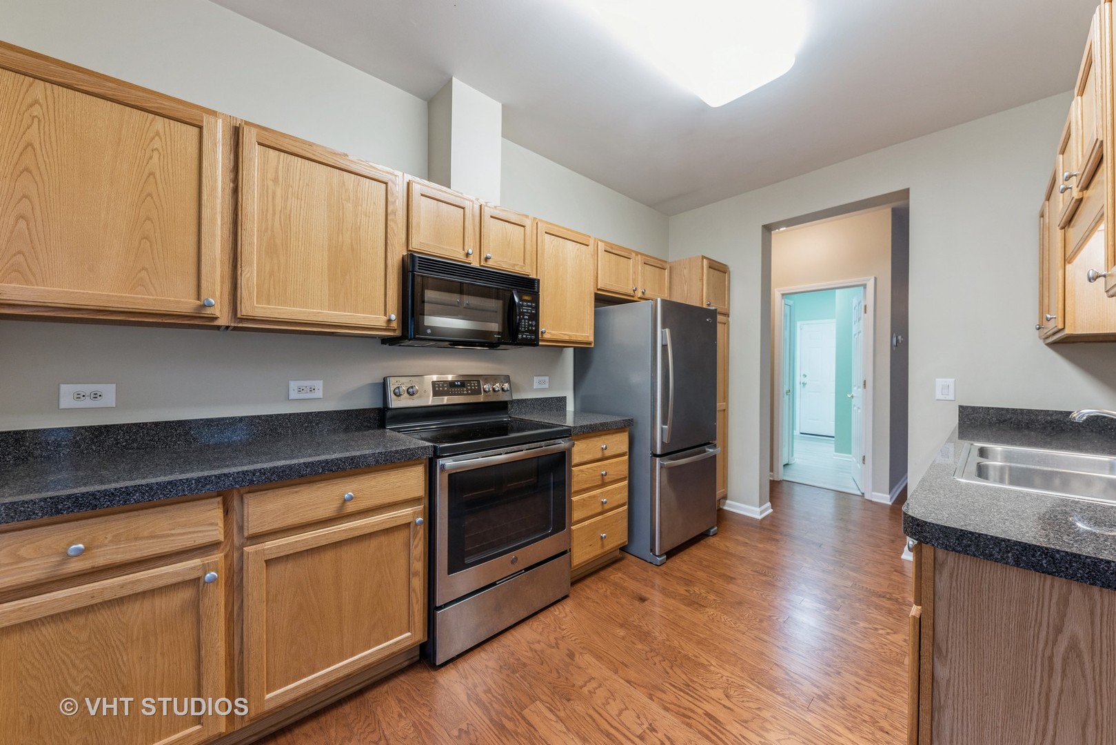 Kitchen with oak cabinets, dark countertops, stainless steel appliances, and wood flooring.