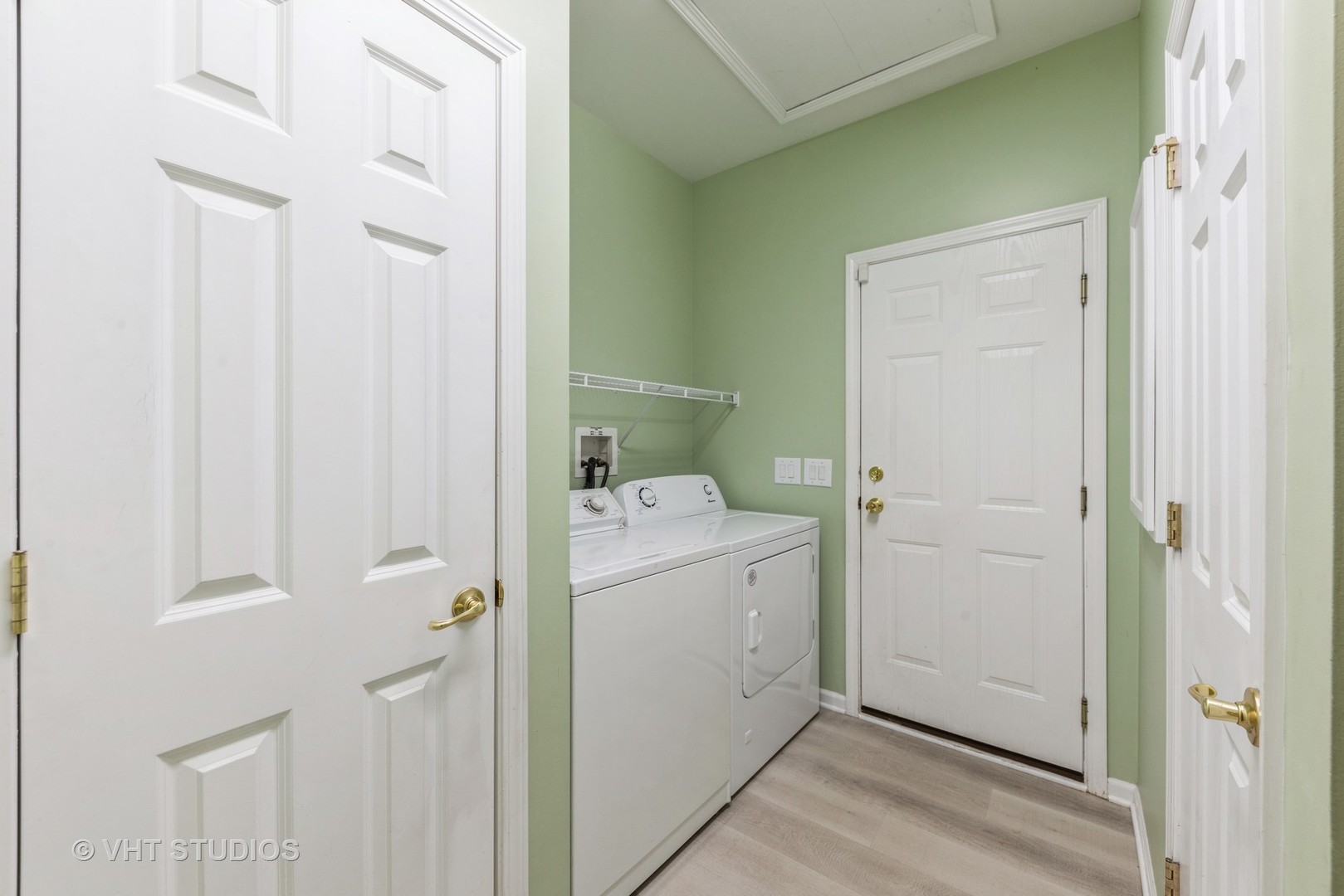 Laundry room with white washer and dryer, wire shelf, pale green walls, and light flooring.