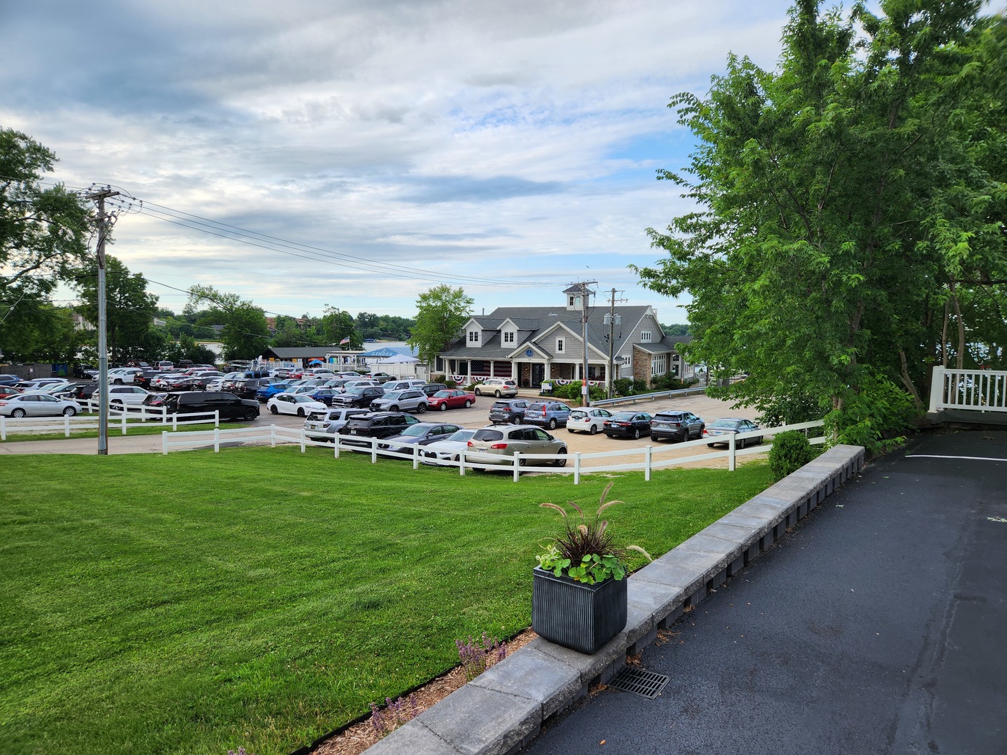 Gabled building beside a large parking lot, seen beyond a curved white fence and grassy lawn.