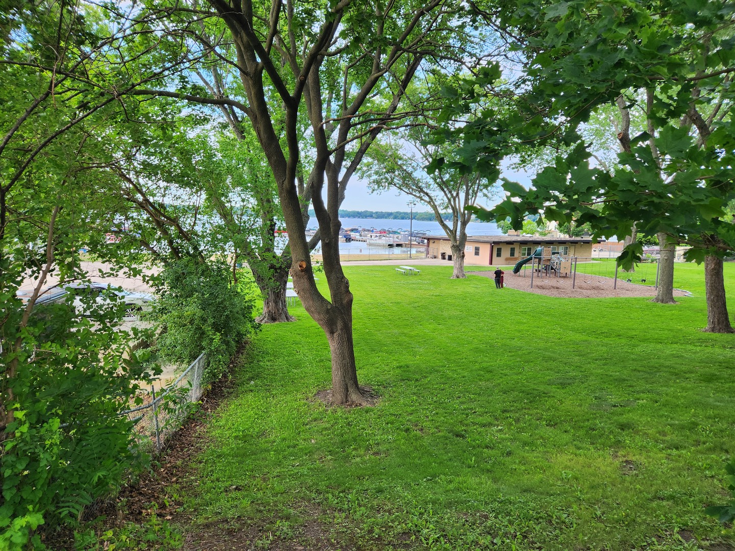Lakeside park with a playground and broad lawn beneath mature trees.
