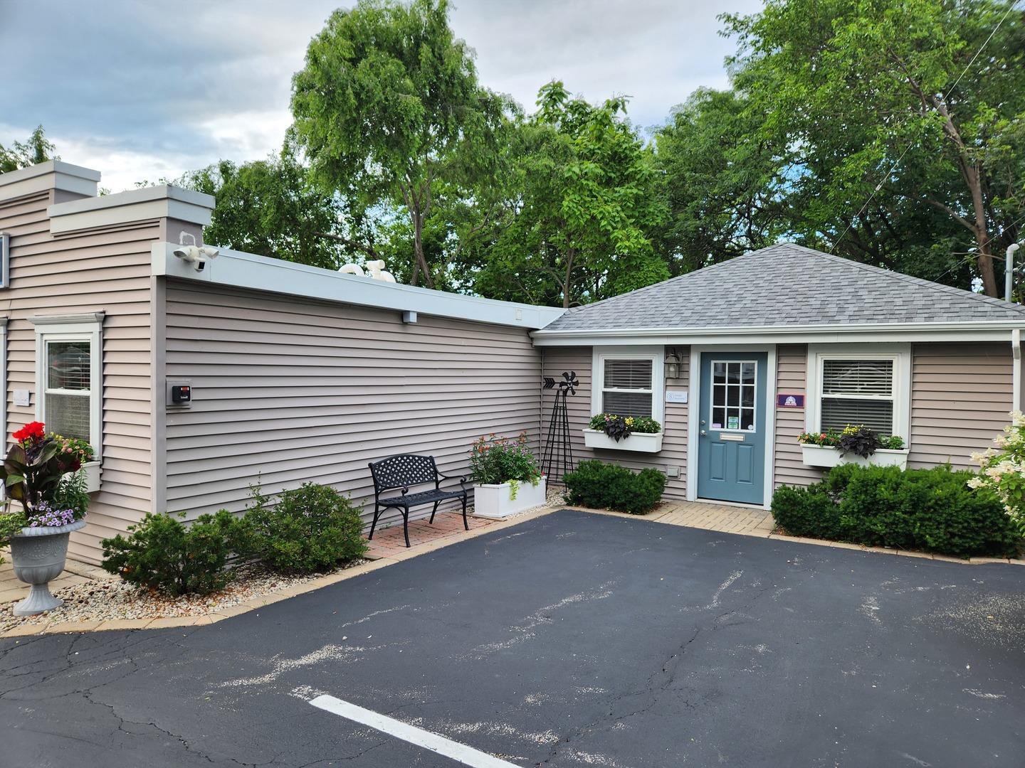 Building entrance with a blue door, flower boxes, and paved parking area.