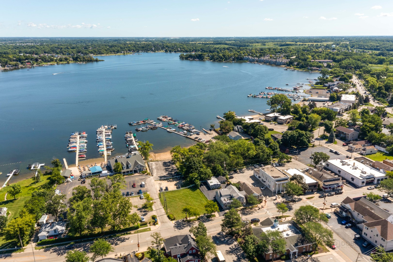 Aerial view of a lakeside town with marinas, boats, and tree-lined streets.