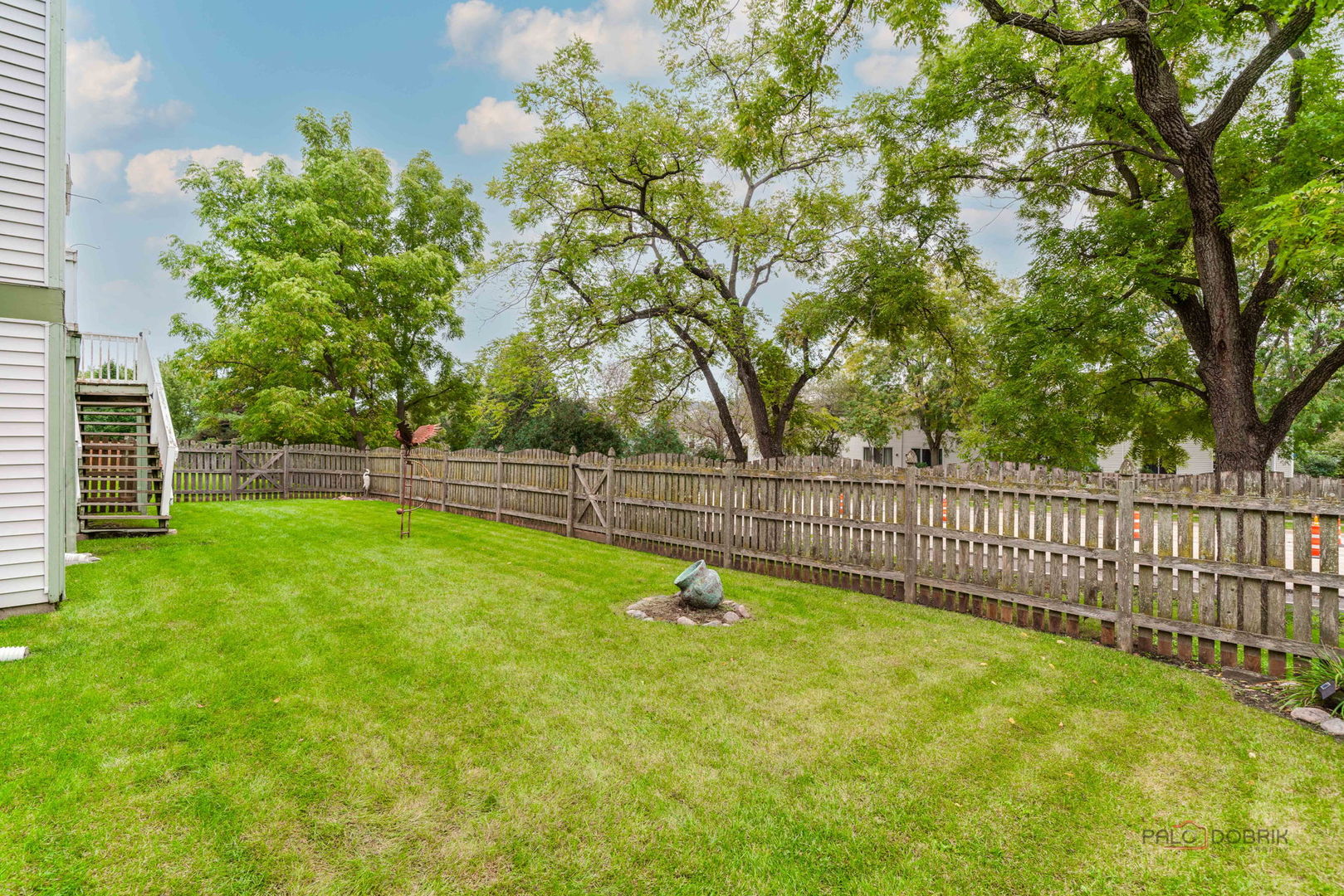 Fenced backyard with a broad lawn, mature trees, and stairs leading to a raised deck.