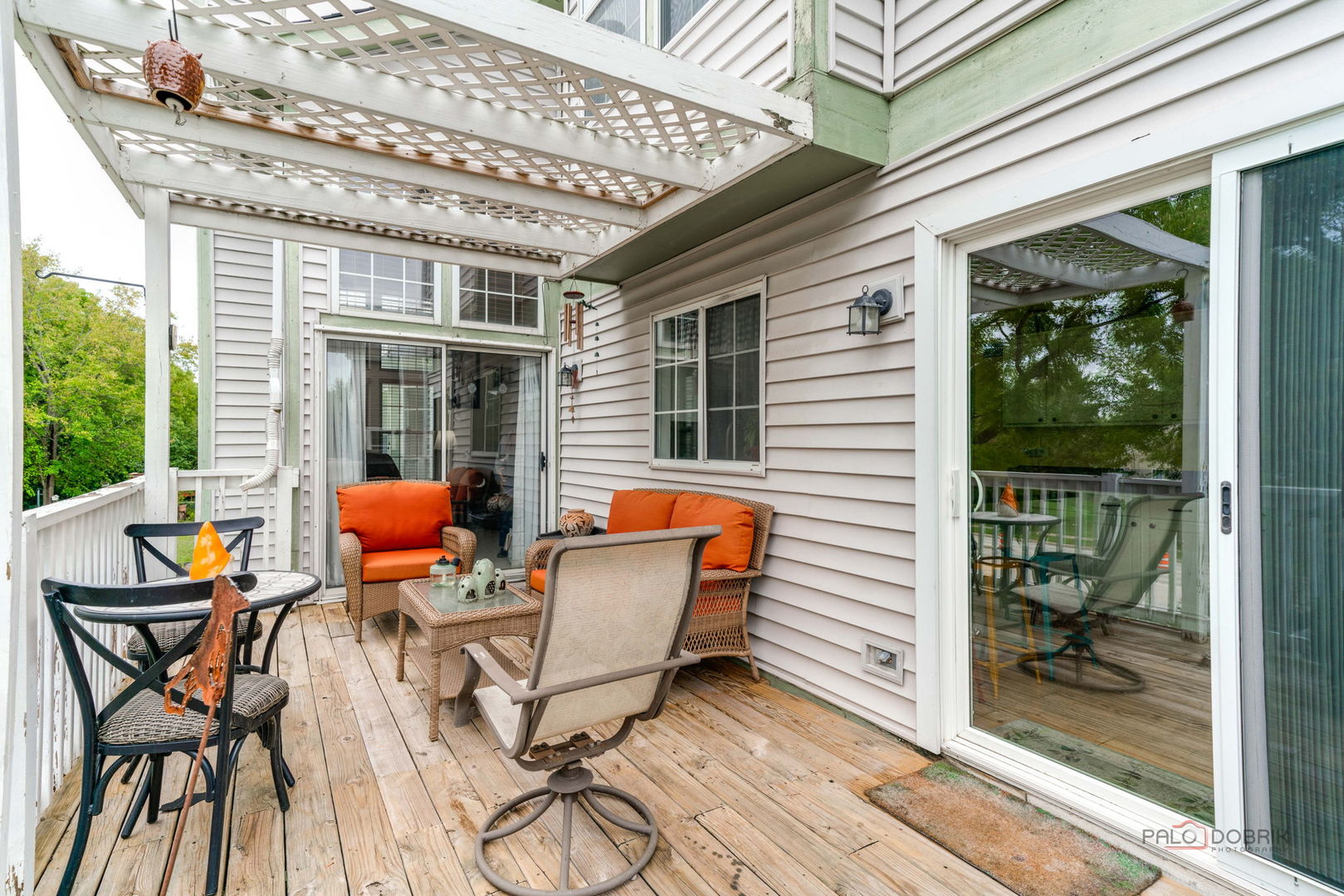 Covered wooden deck with lattice pergola, wicker seating, and bright orange cushions.