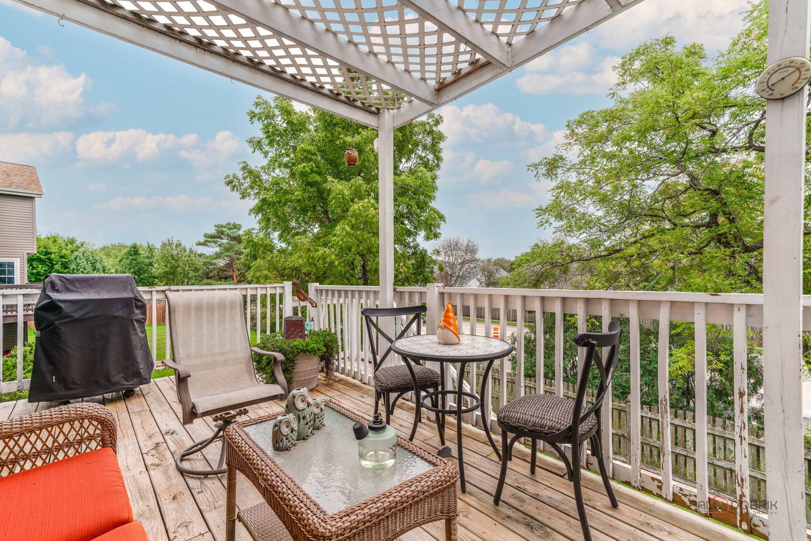 Wooden deck under a lattice pergola with outdoor dining furniture and a covered grill.
