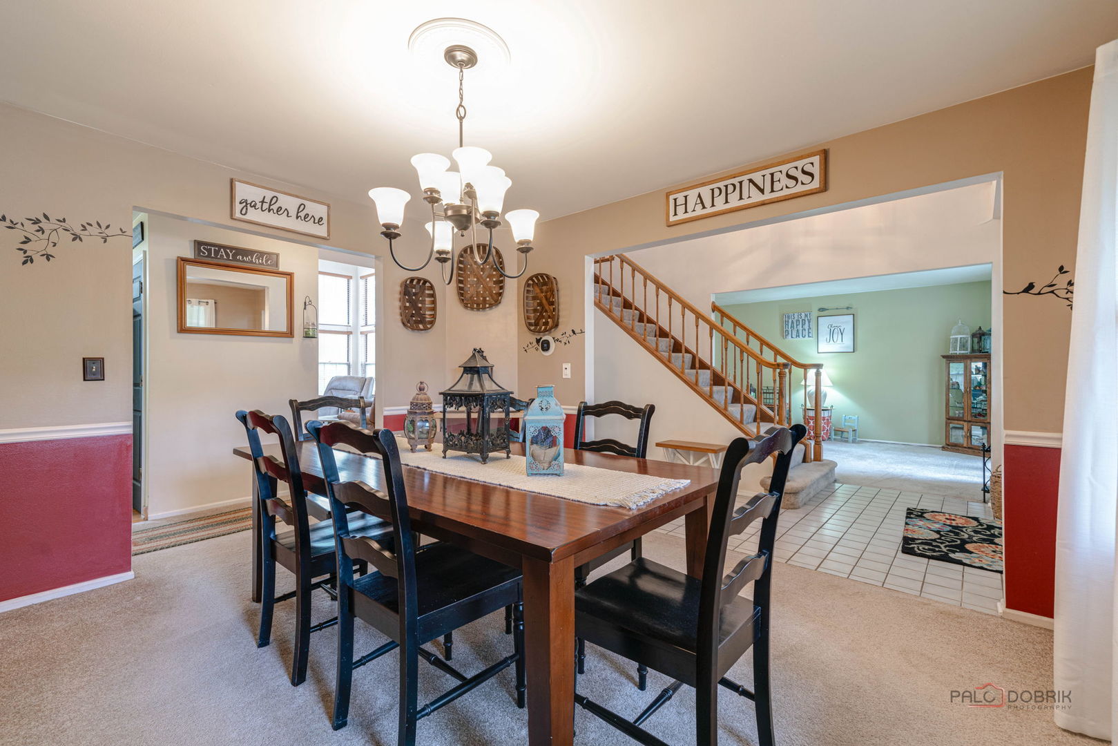 Dining room with a dark wood table, black chairs, and a chandelier beside an open staircase.