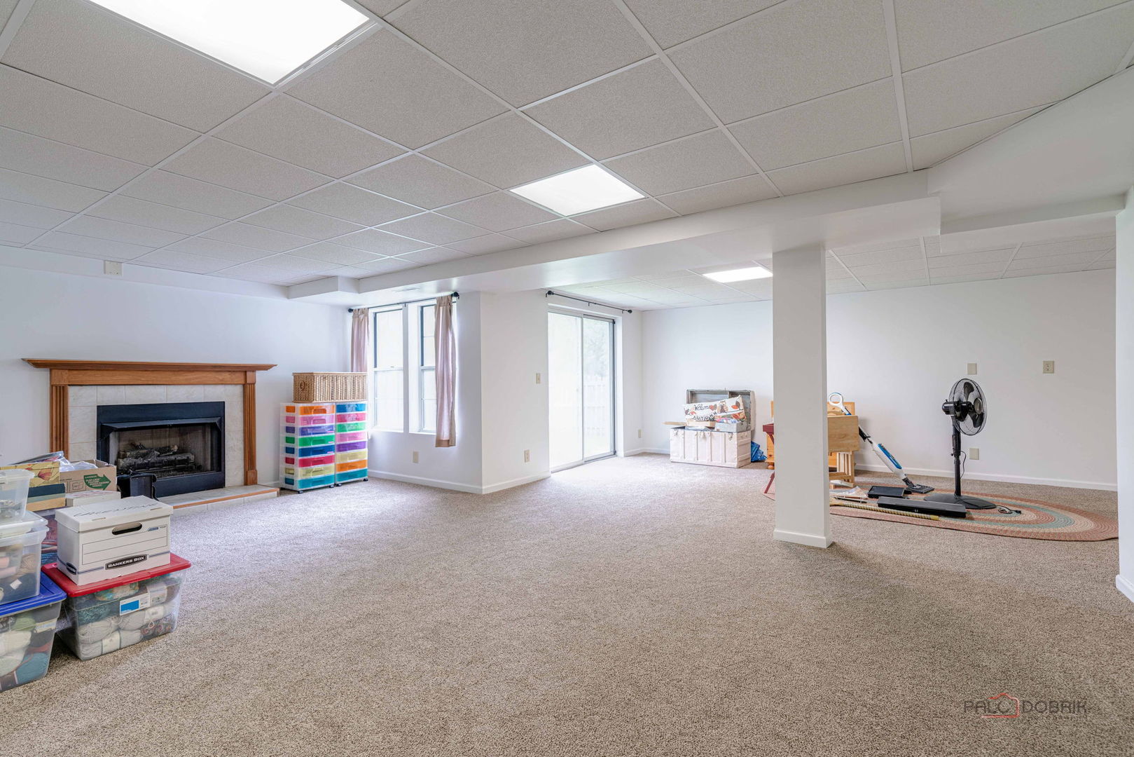 Carpeted living area with a wood-trimmed fireplace, sliding glass door, and storage bins.