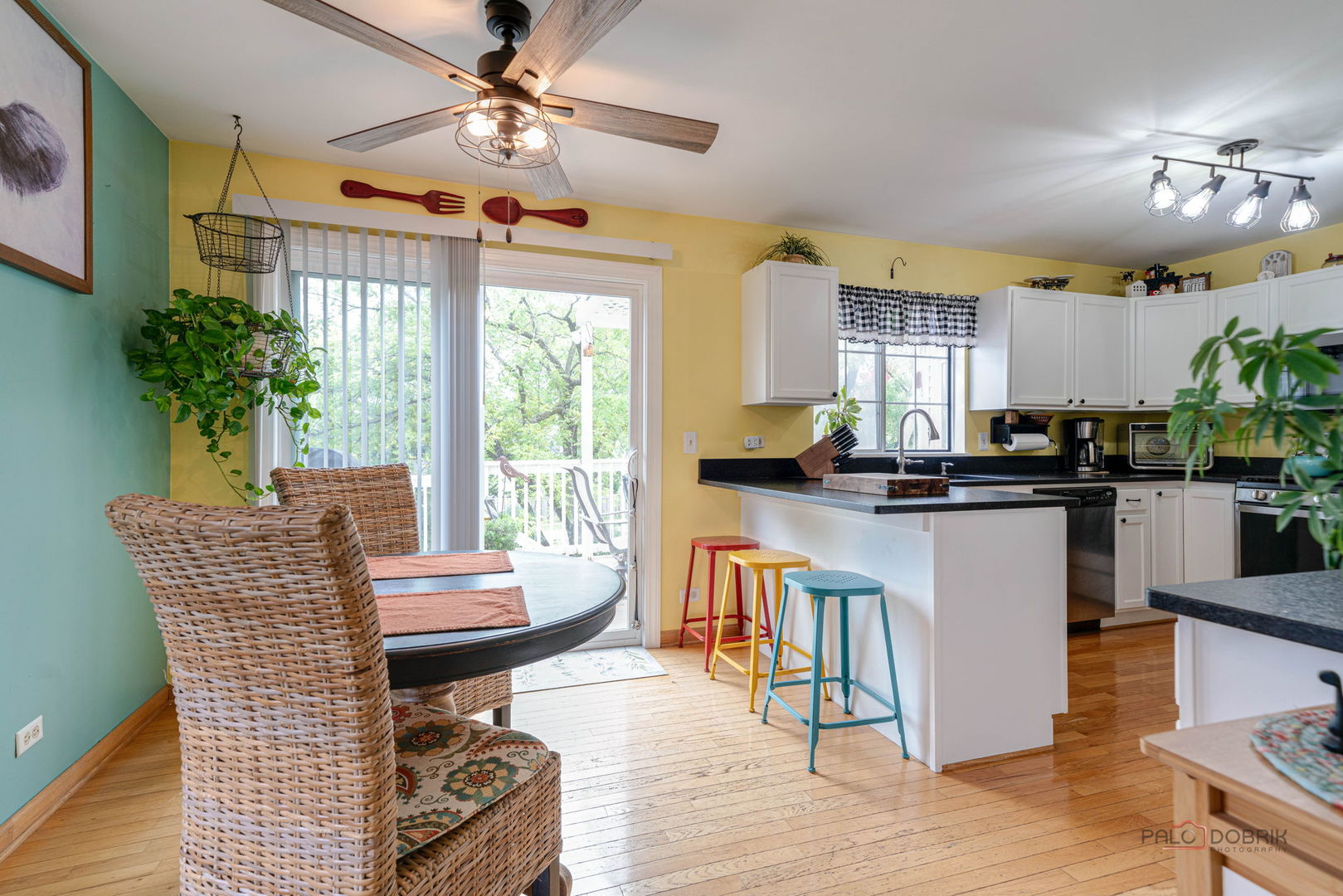 Kitchen and dining nook with colorful bar stools, wicker chairs, and sliding glass doors to a deck.