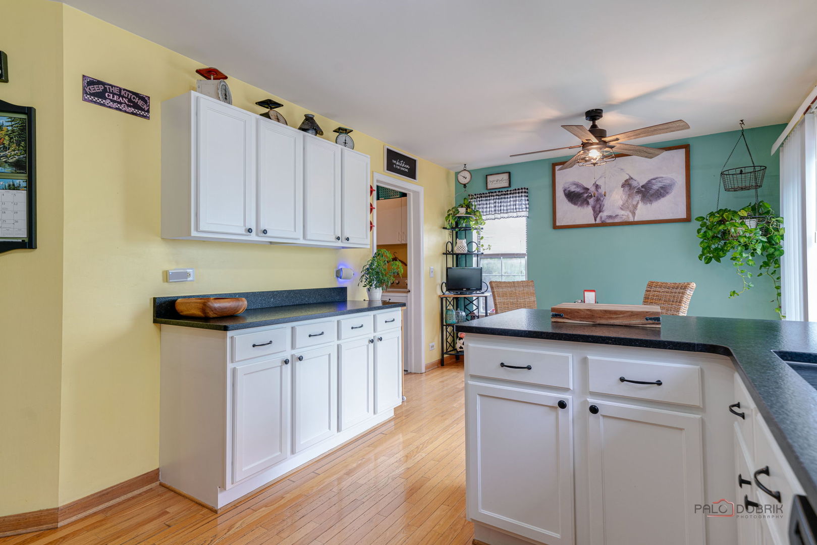 Kitchen with white cabinetry, dark countertops, hardwood floors, and a teal dining area.