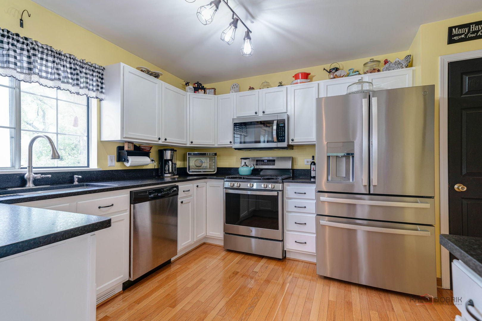 Kitchen with white cabinets, stainless steel appliances, and a large window above the sink.