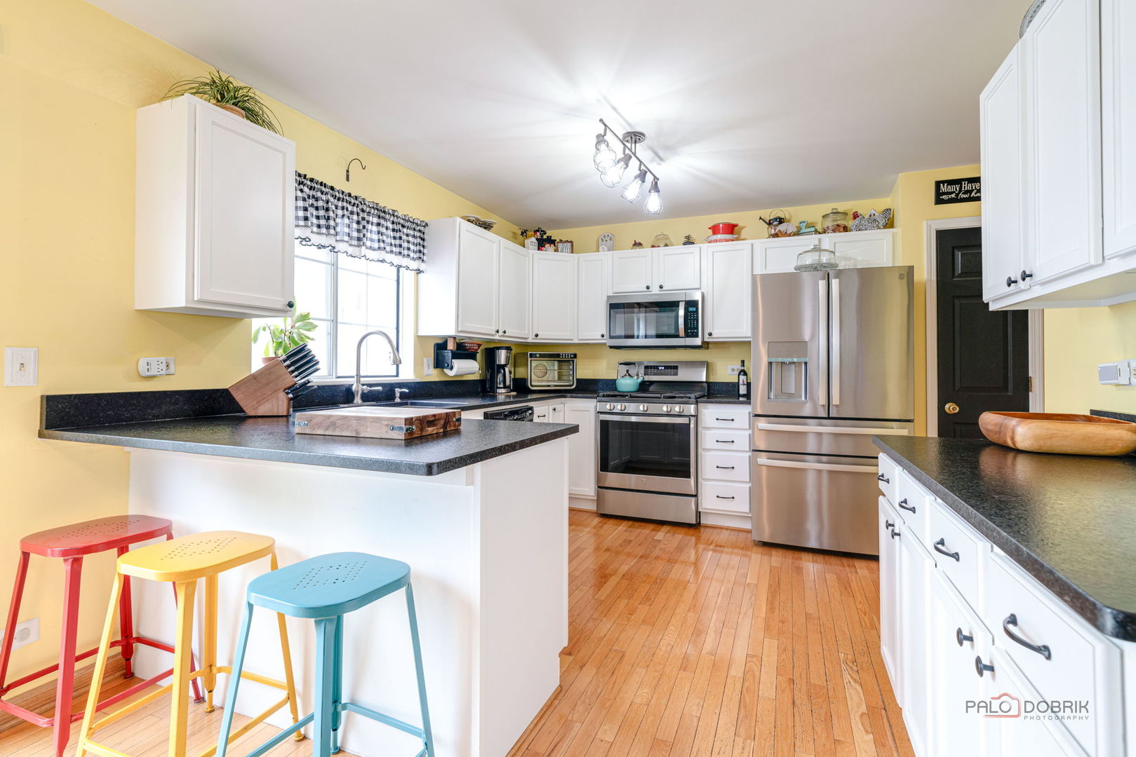 Kitchen with white cabinets, stainless steel appliances, dark countertops, and colorful stools at the breakfast bar.