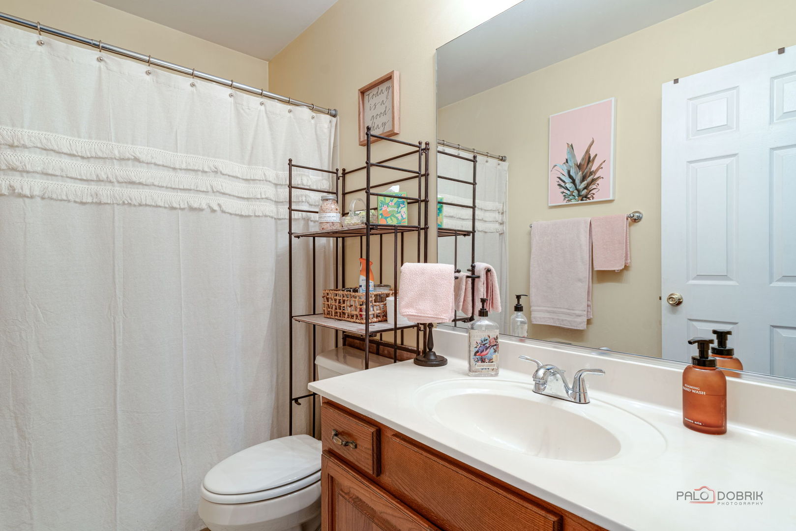 Bathroom with a wood vanity, white countertop, shower curtain, and black metal storage rack.