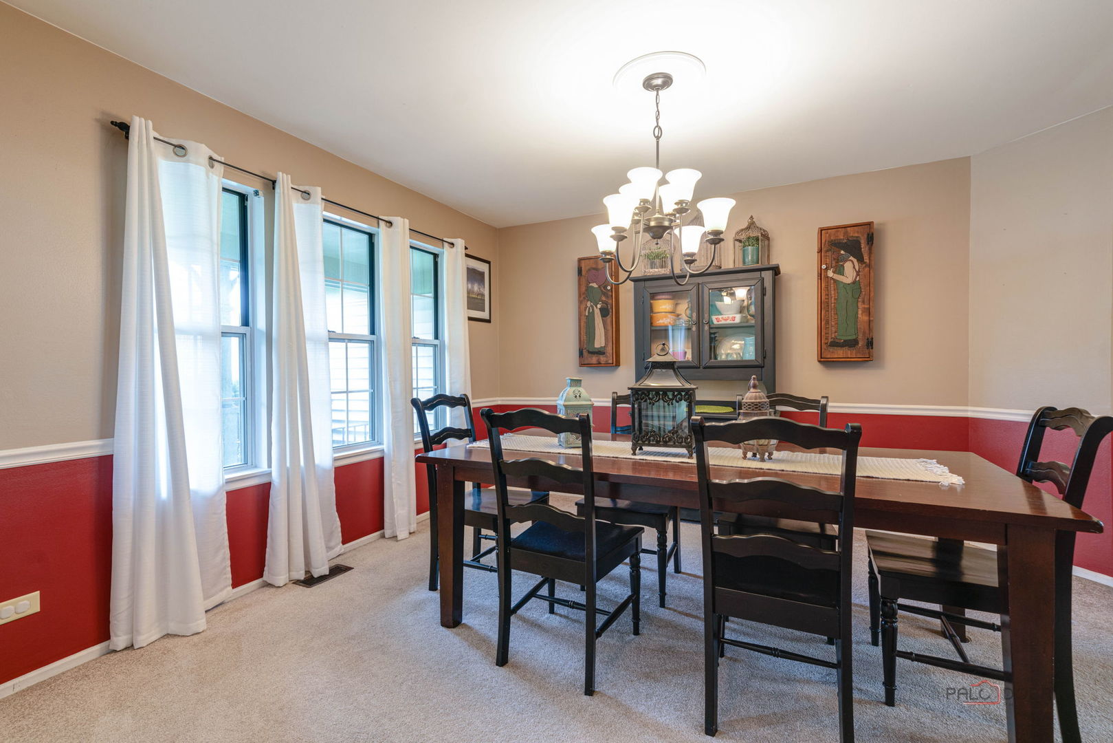 Furnished dining room with a dark wood table, chandelier, tall curtained windows, and red wainscoting.