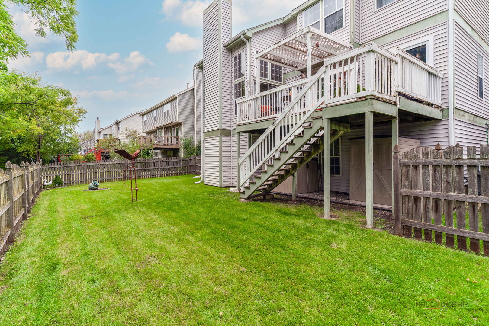 Fenced backyard with a broad lawn and a raised deck with stairs and pergola.
