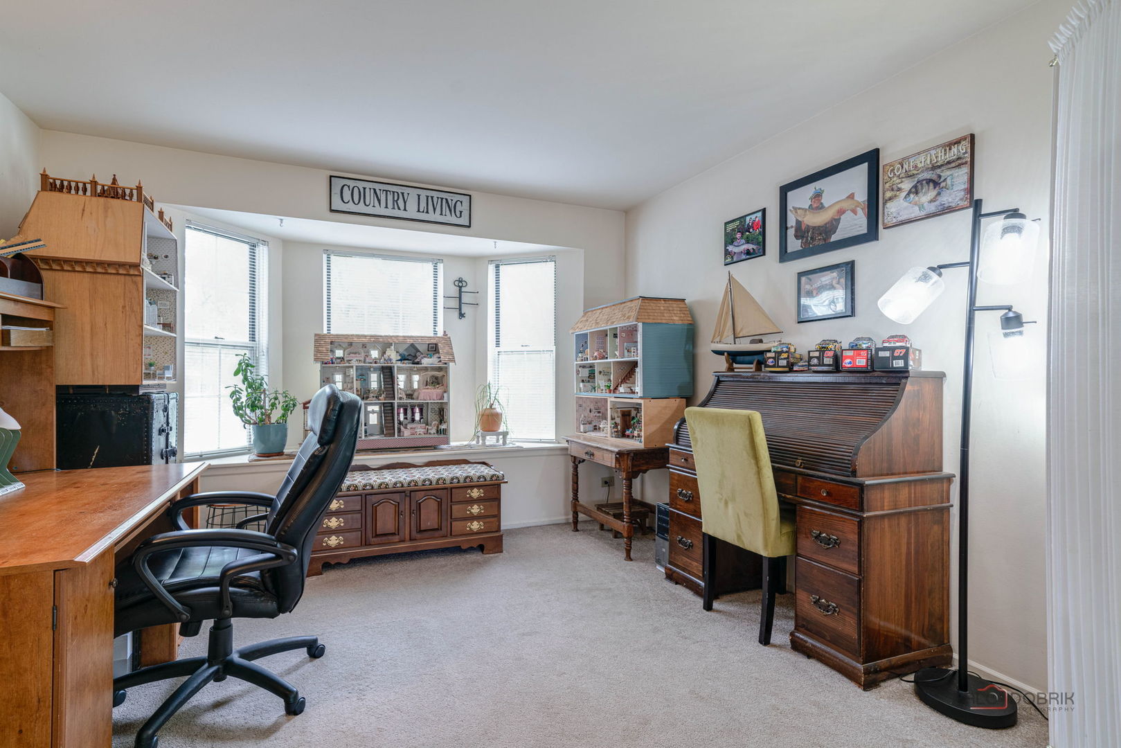 Home office with wooden desks, displayed dollhouses, and fishing-themed pictures.