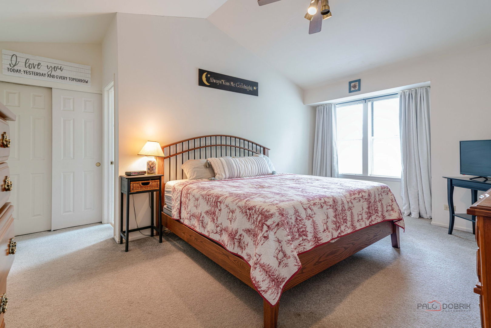 Furnished bedroom with a wooden bed, patterned bedspread, and large curtained window.