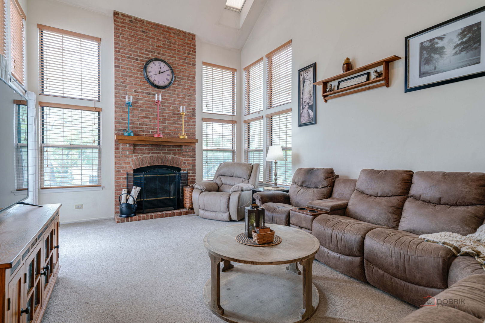 Living room with tall windows, a brick fireplace, and a brown sectional sofa.