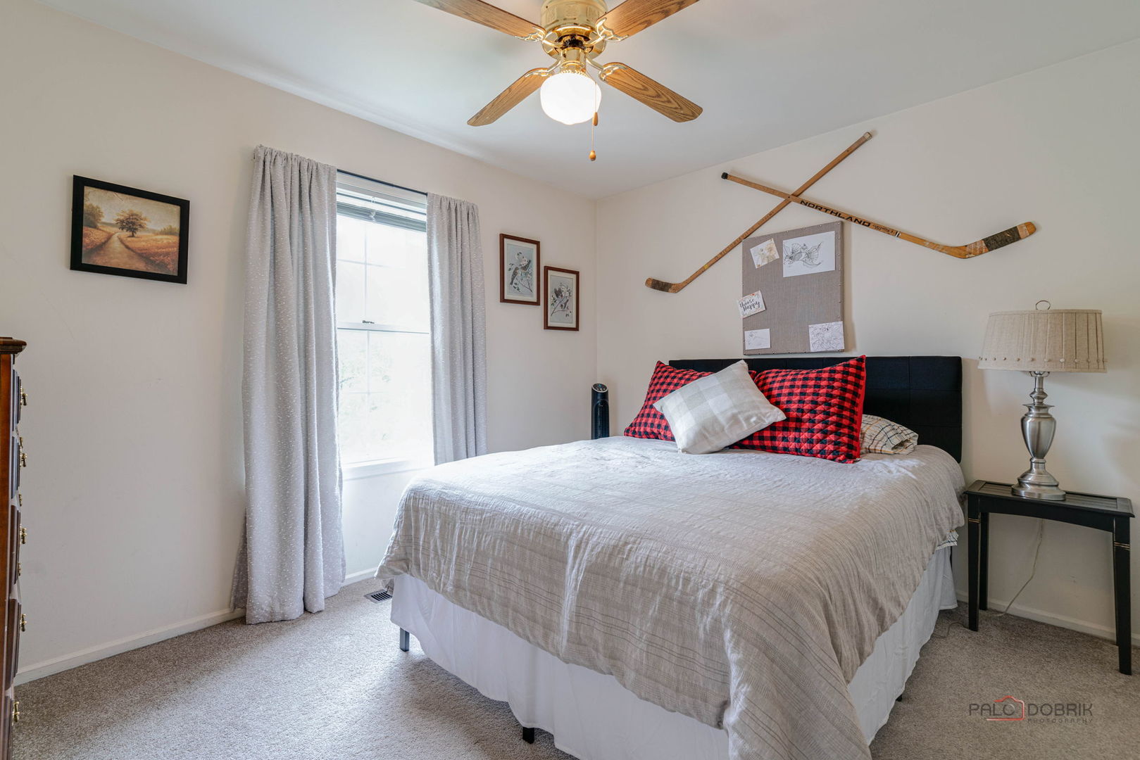 Bedroom with a gray-covered bed, plaid pillows, and crossed hockey sticks above the headboard.