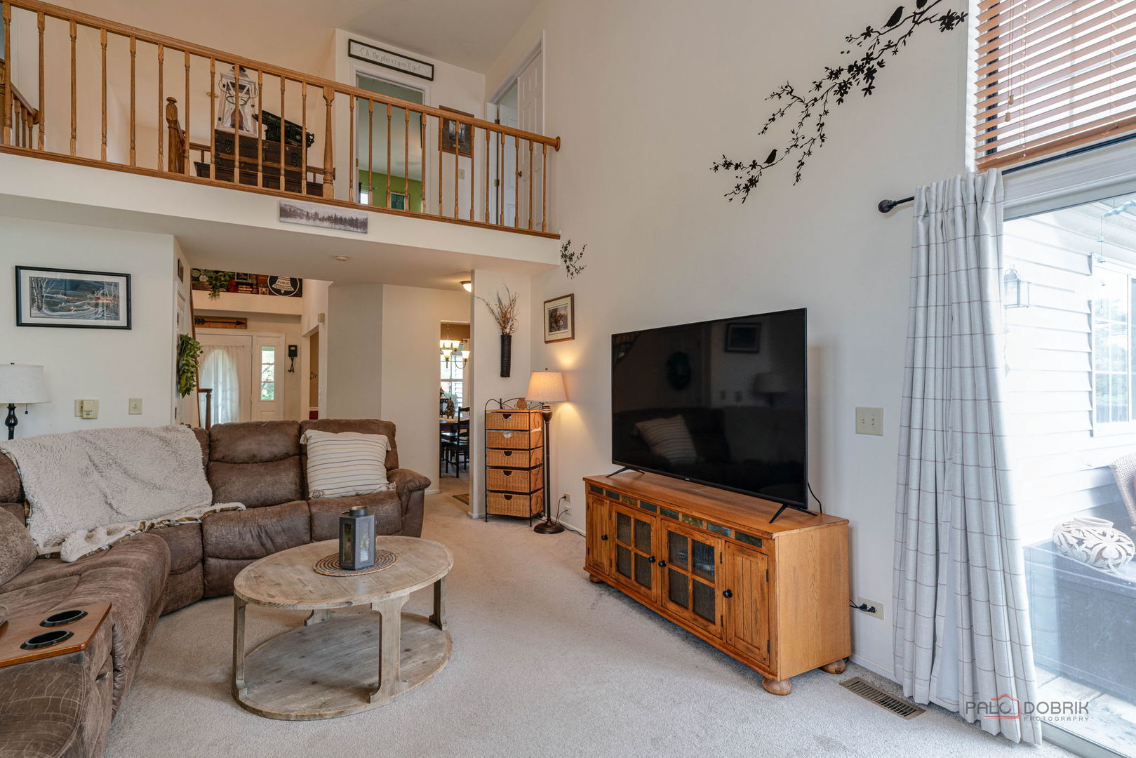 Living room with open loft, wood railing, sectional sofa, and sliding glass doors.