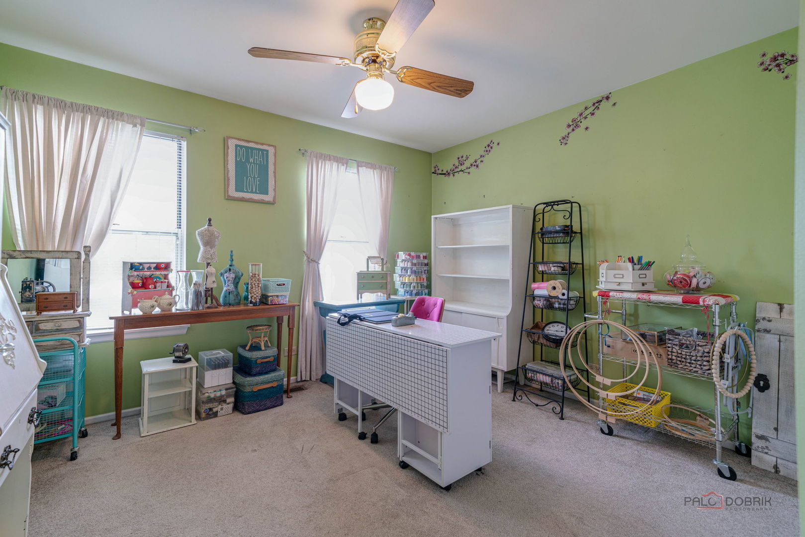Craft room with green walls, sewing tables, shelves, and a ceiling fan.