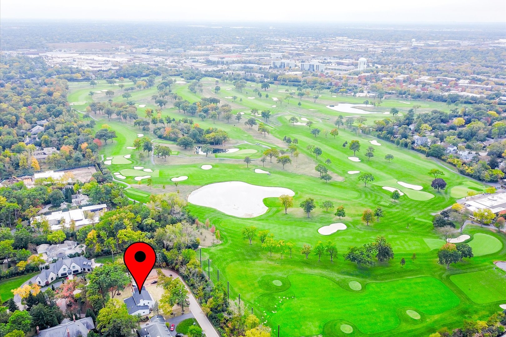 Aerial view of a home beside a golf course, marked with a red location pin.