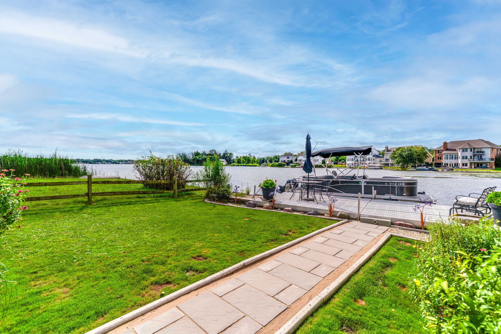 Waterfront backyard with a stone path leading across the lawn to a dock and pontoon boat.