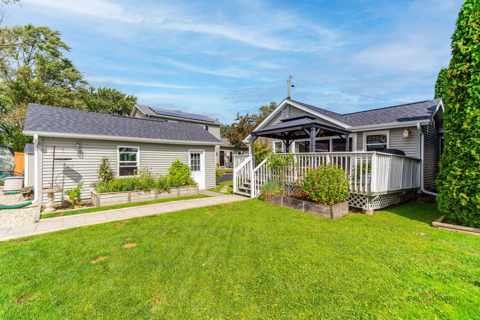 Gray-sided home with a covered deck, raised garden beds, and a broad green lawn.