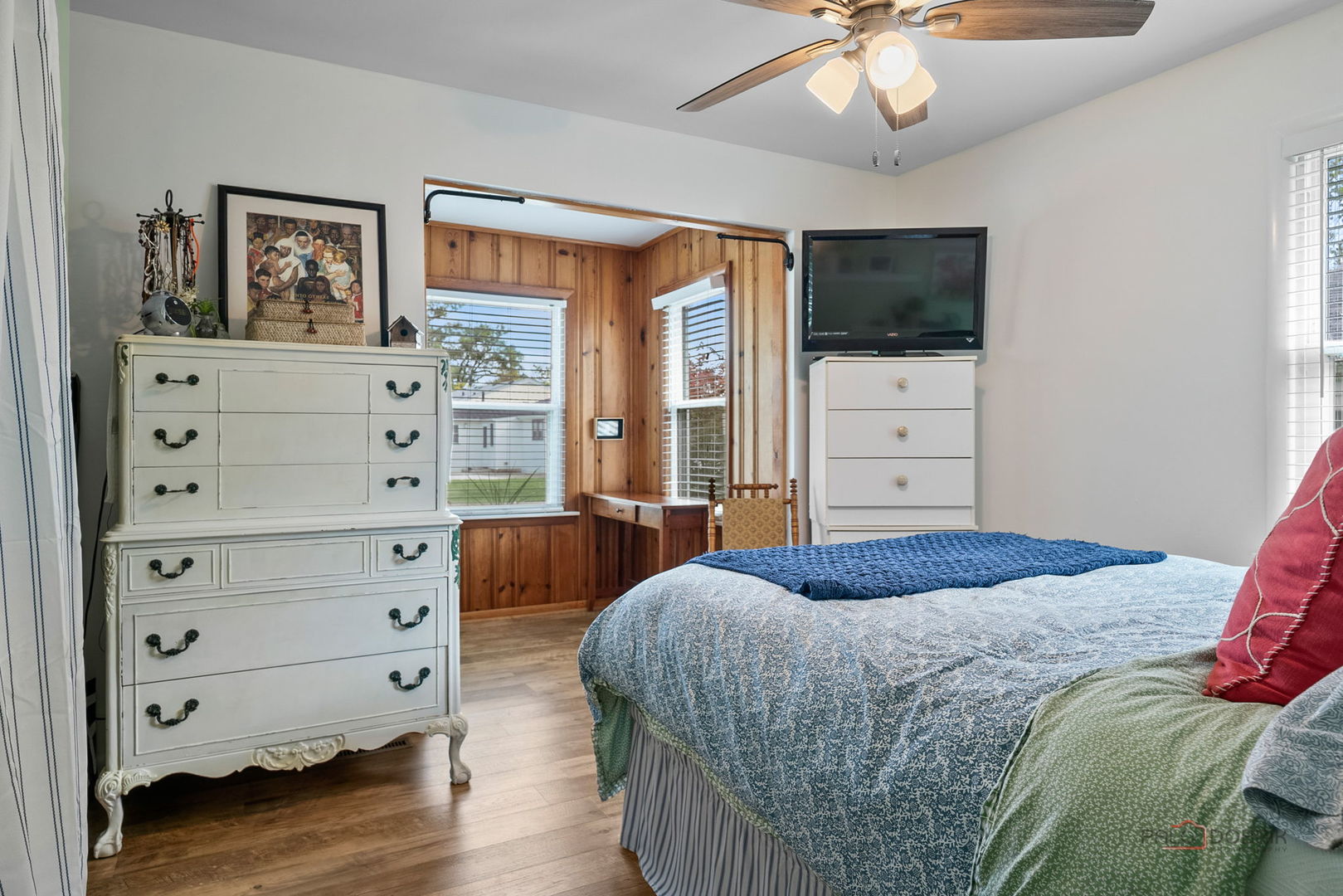 Furnished bedroom with a blue-patterned bedspread and a wood-paneled window nook.