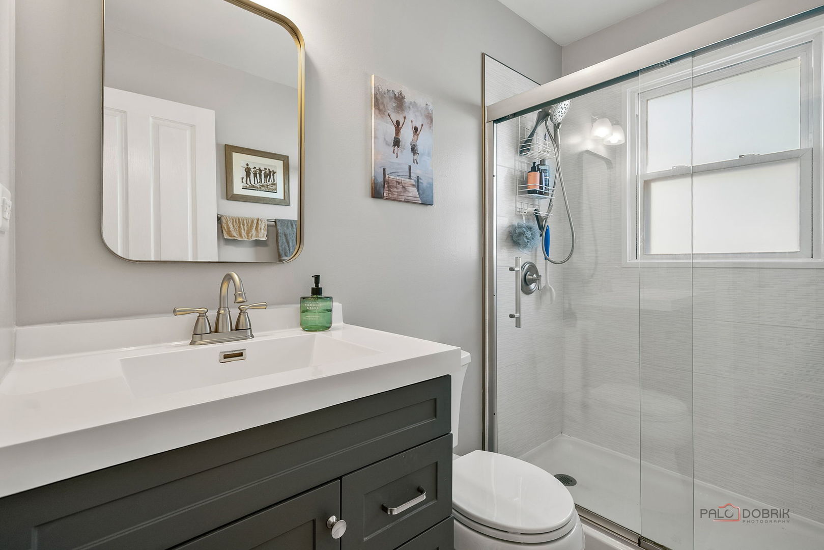 Bathroom with a dark gray vanity and a glass-enclosed shower beside a window.