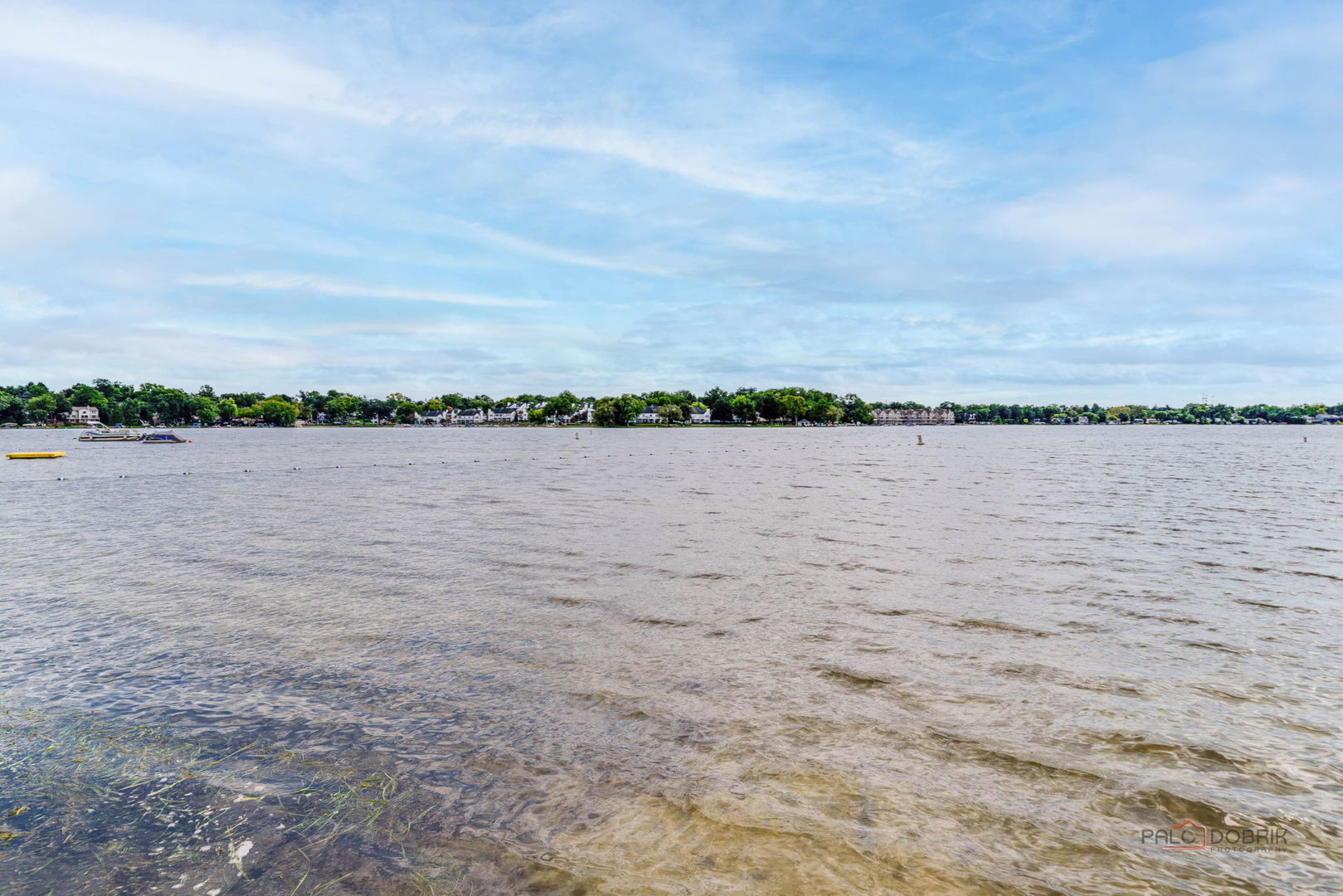 Panoramic lake view with shallow water, buoys, and homes along the distant shoreline.
