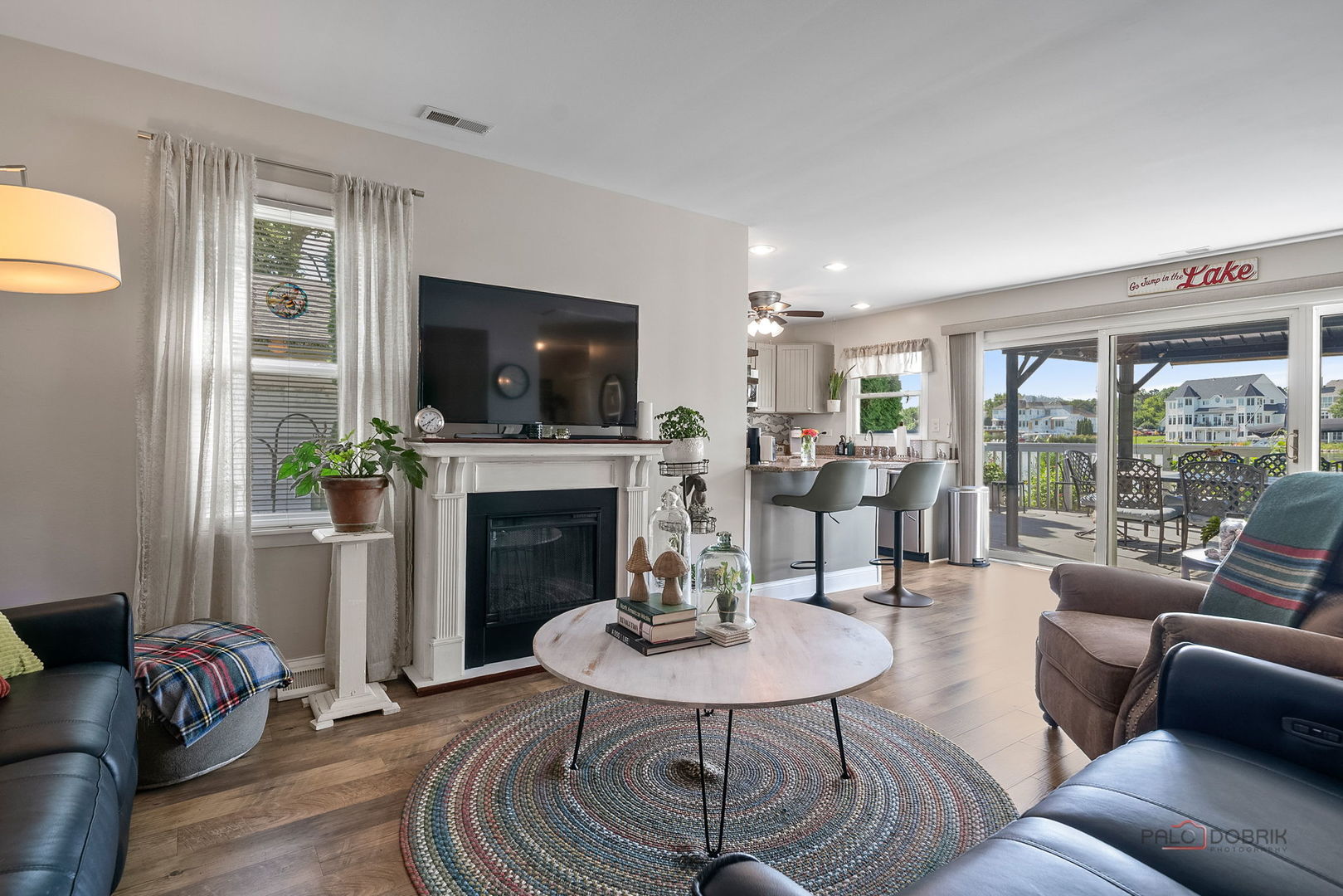 Living room with a white fireplace, round coffee table, and sliding doors to a covered patio overlooking the water.