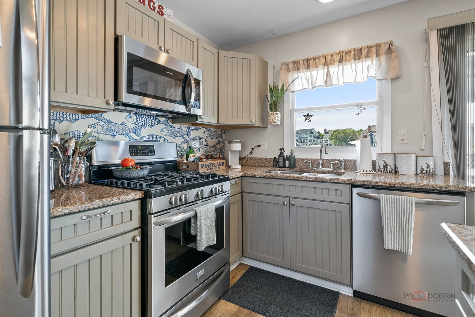 Kitchen with gray paneled cabinets, stainless steel appliances, granite counters, and a blue fish-patterned backsplash.