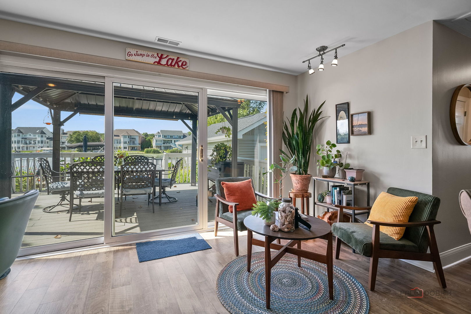 Living room opens onto a covered deck overlooking the water, with green armchairs and a round coffee table.