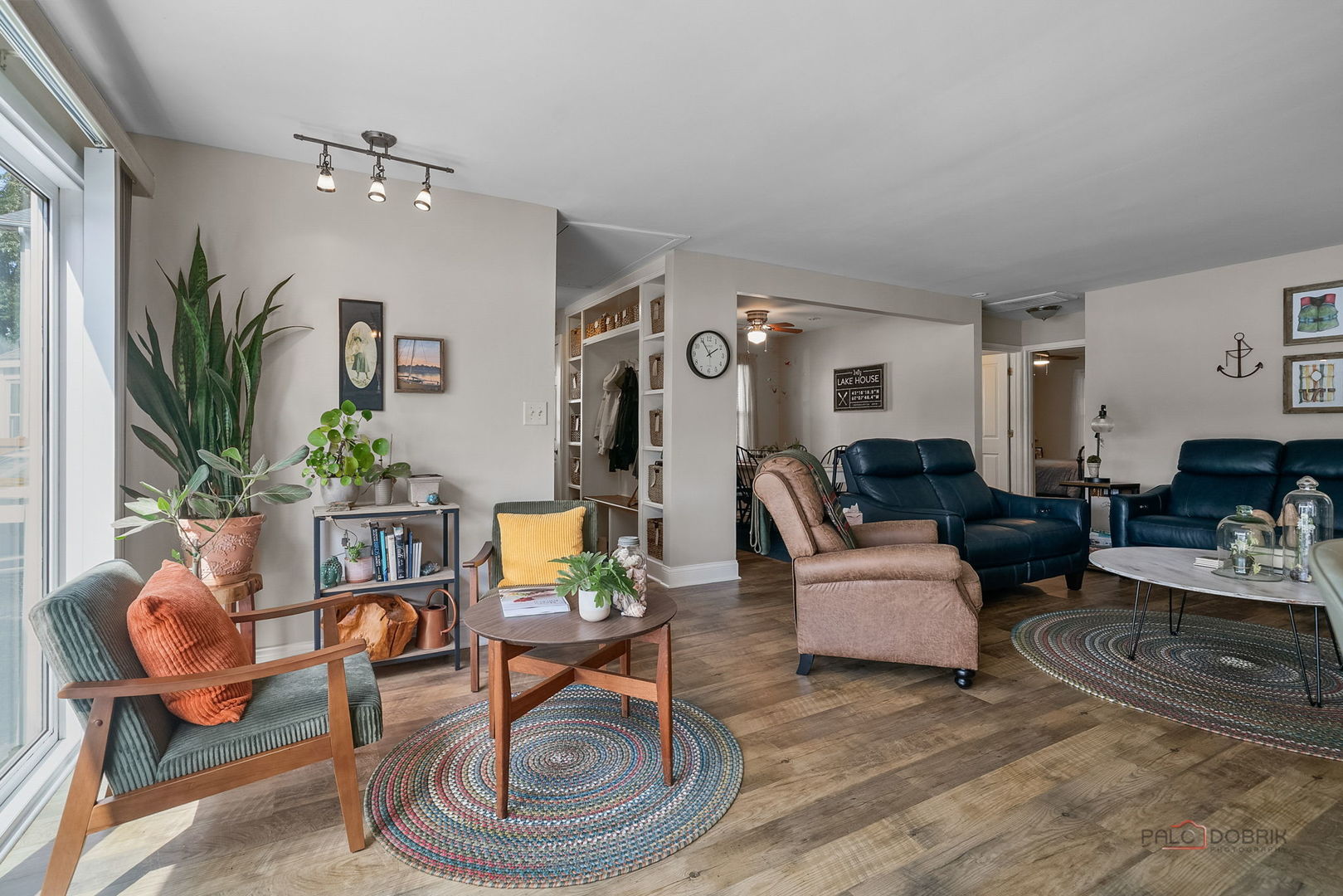 Living room with dark blue sofas, colorful braided rugs, and large windows.