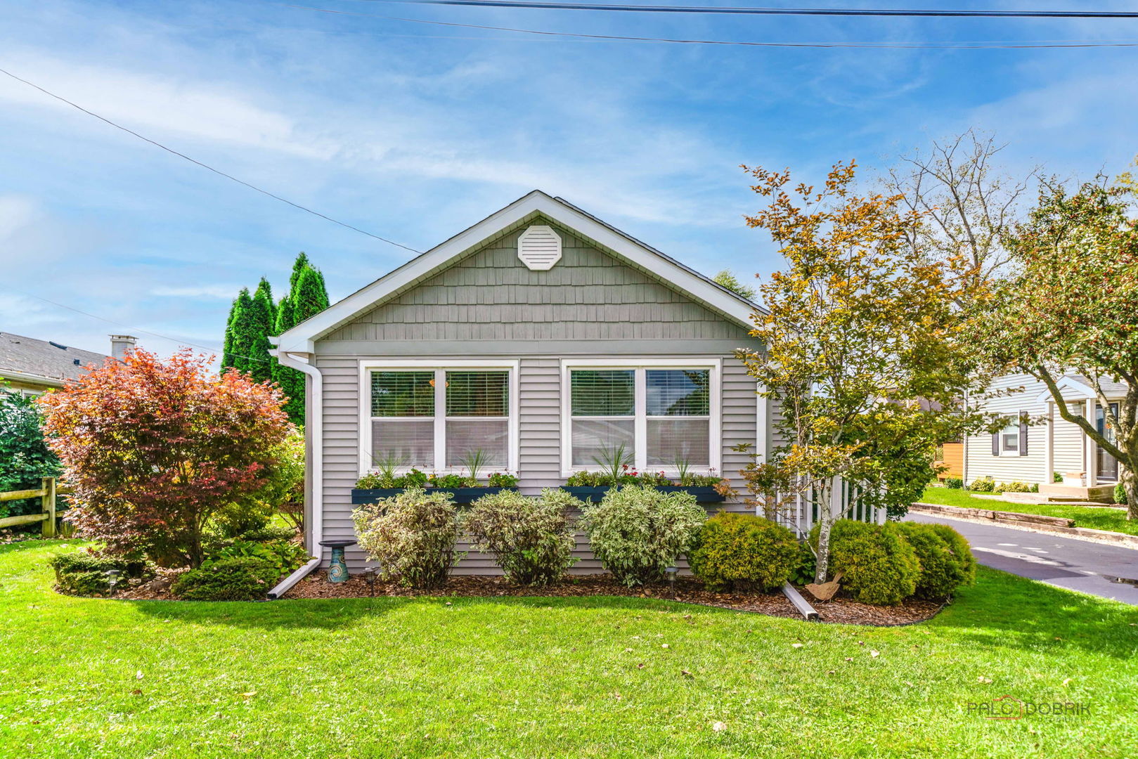 Gray-sided home's front facade with broad windows, landscaped shrubs, and green lawn.