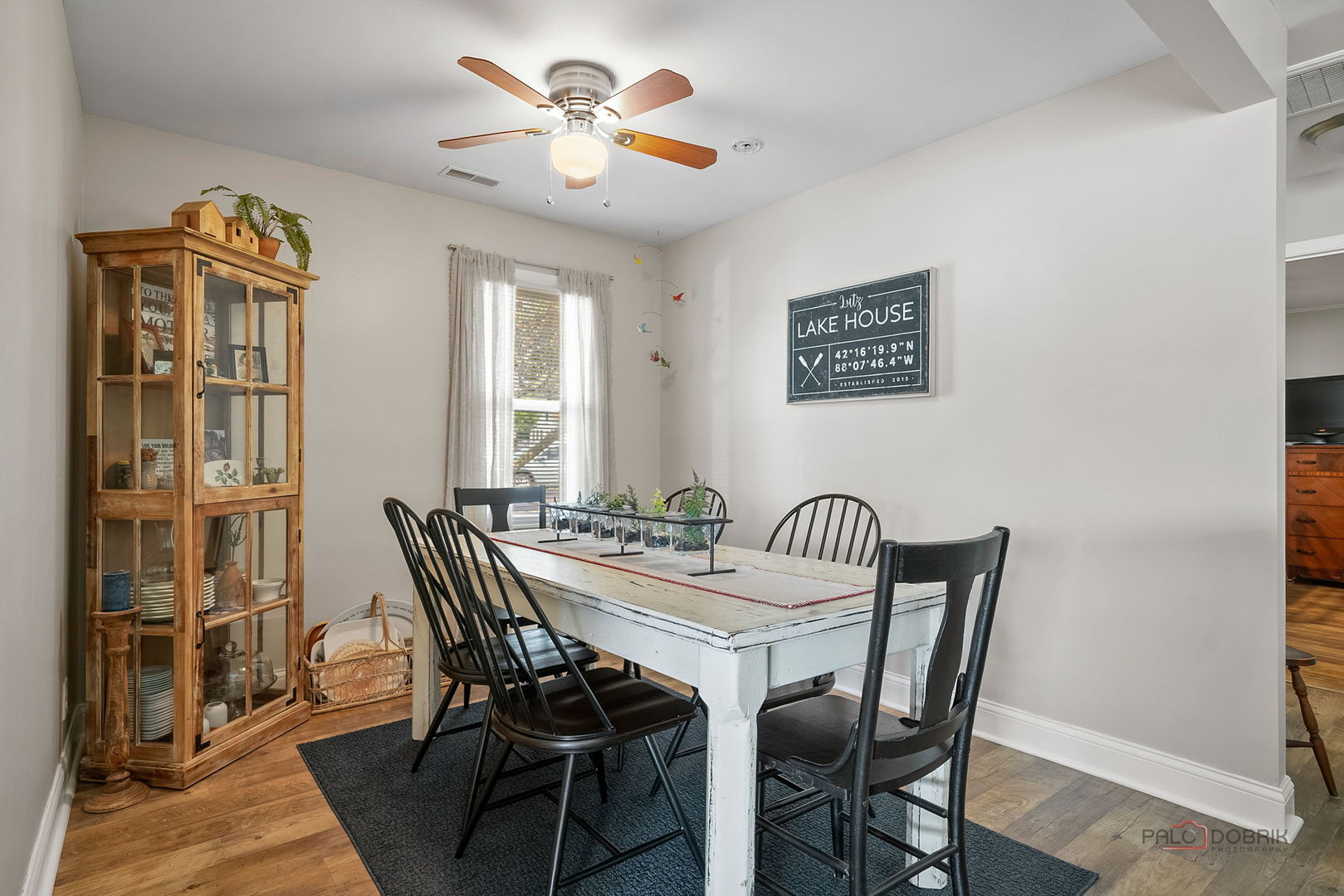 Dining room with a distressed farmhouse table, black chairs, and a wooden glass-front cabinet.