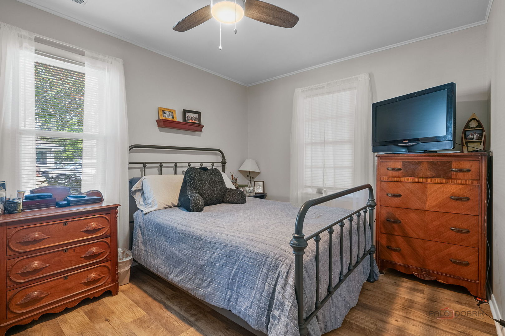 Furnished bedroom with a metal bed, two windows, and wooden dressers.
