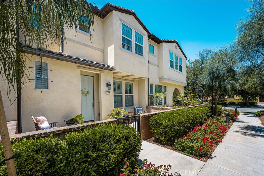 Two-story townhouse with a small gated patio, manicured hedges, and red flowering plants.