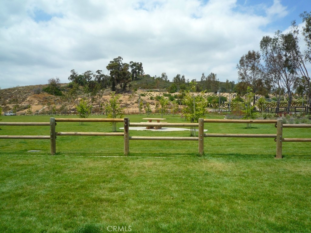 Grassy park with a wooden rail fence, picnic table, and rolling hills.