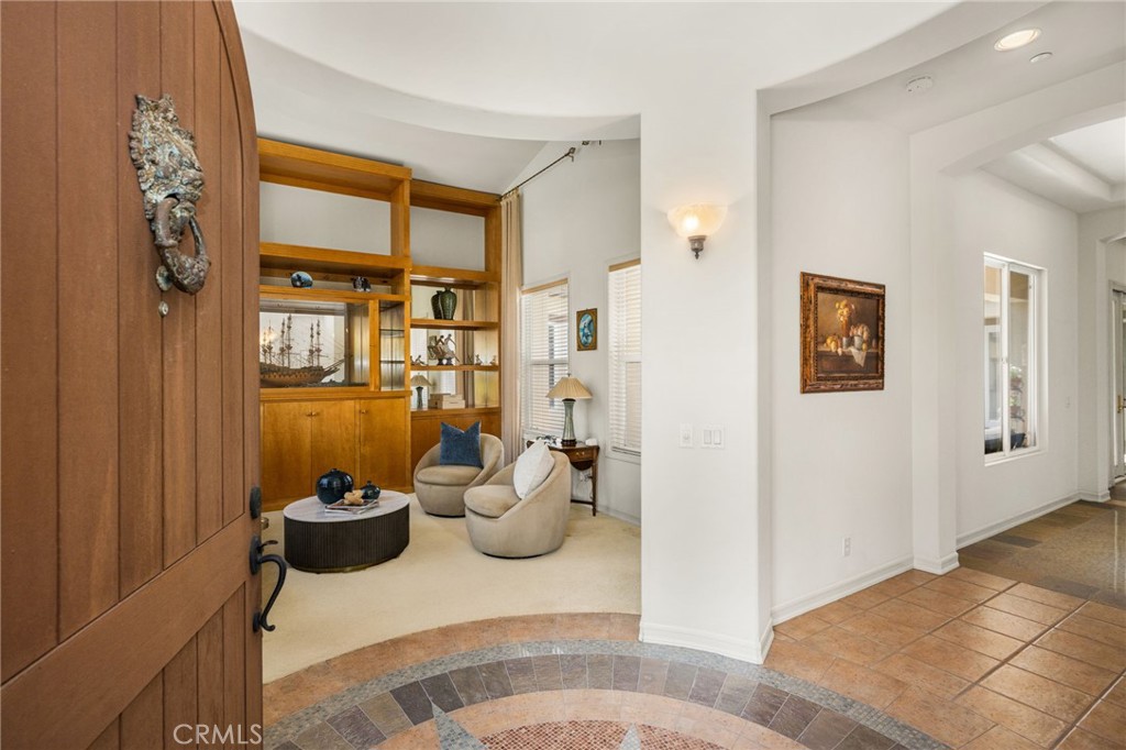 Entryway opening into a sitting room with built-in wood shelving and tiled floor.