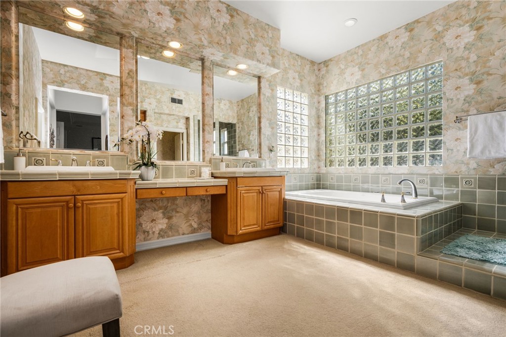 Bathroom with wood vanities, mirrored walls, and a tiled soaking tub beside glass-block windows.