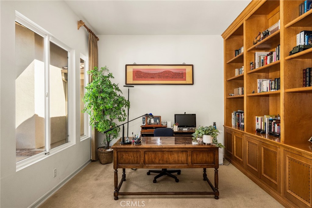 Home office with a wooden desk, built-in bookshelves, and bright windows.
