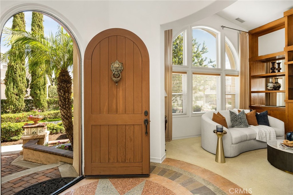 Bright entryway with an open arched wooden front door, garden views, and a curved living room sofa.
