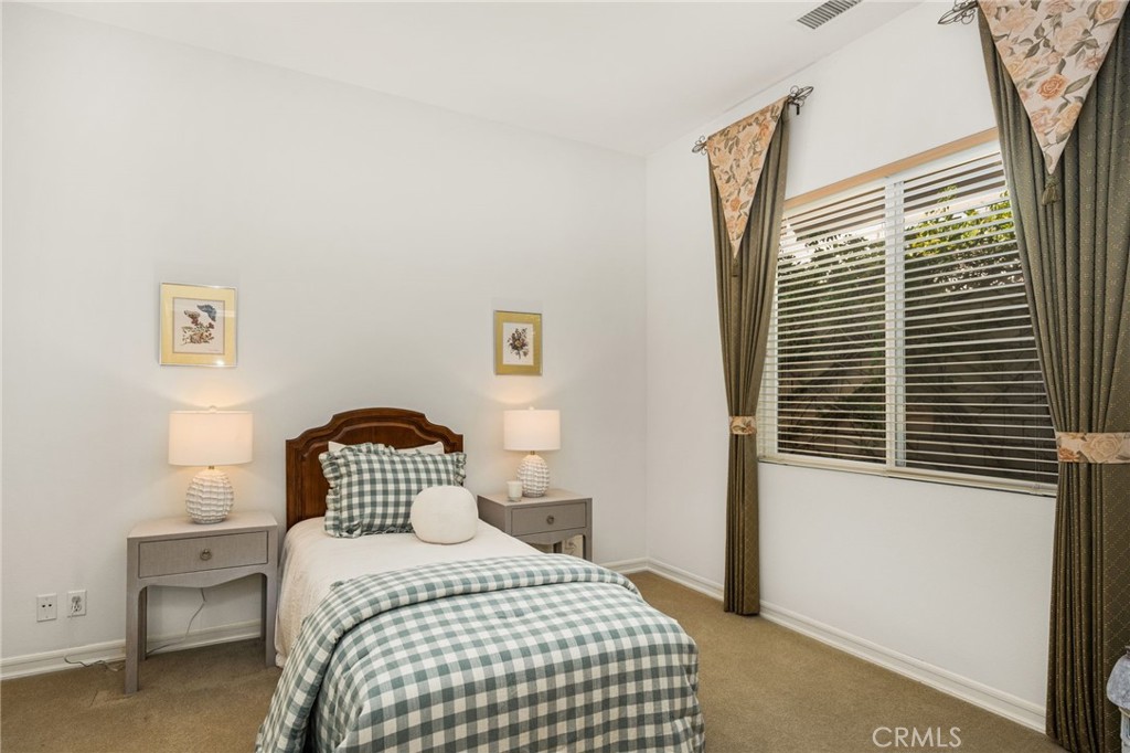 Bedroom with a neatly made bed, matching bedside tables, and a large curtained window.