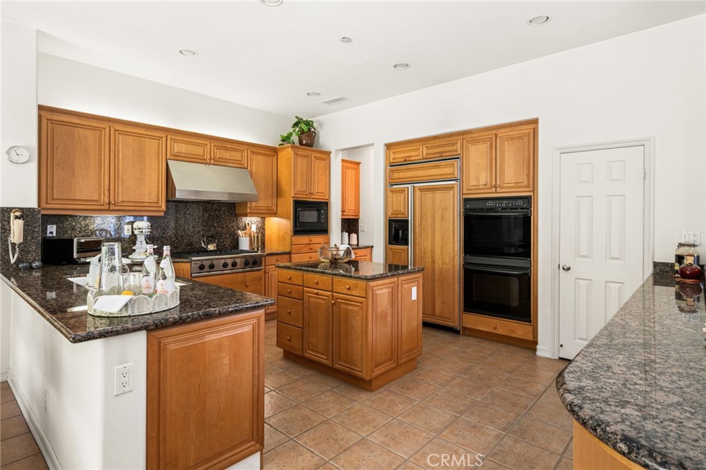 Kitchen with honey-toned wood cabinets, granite counters, a central island, and double ovens.