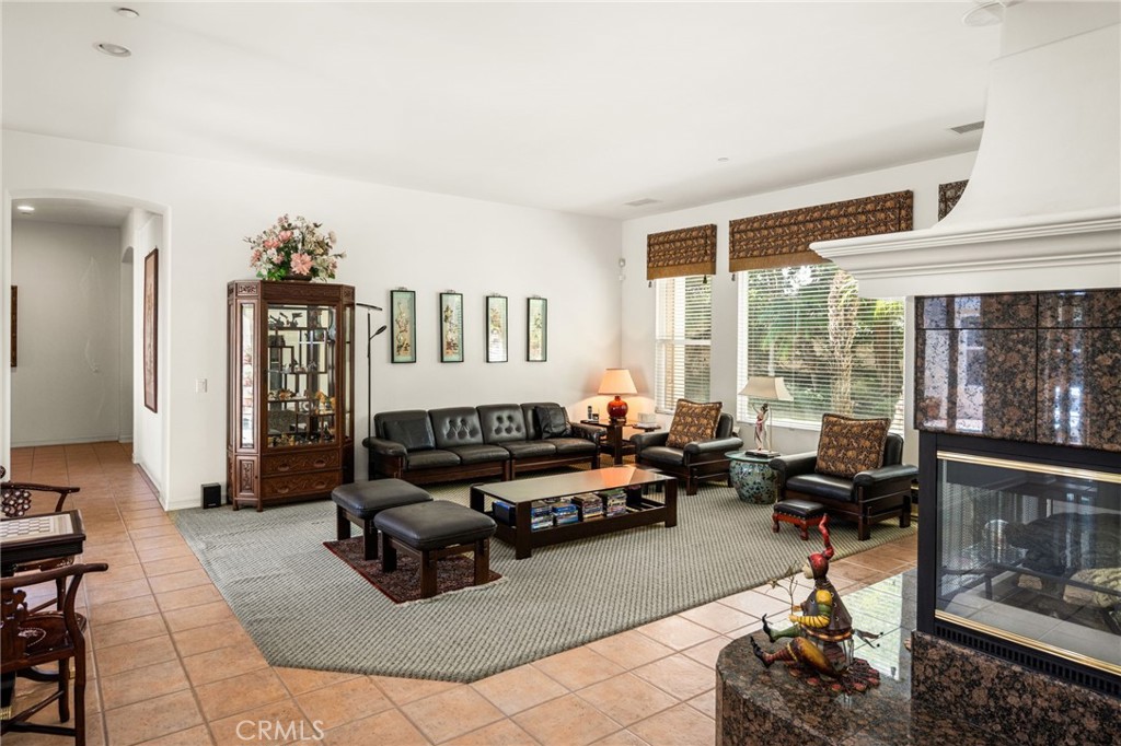 Furnished living room with a stone fireplace, large windows, and tile floors.