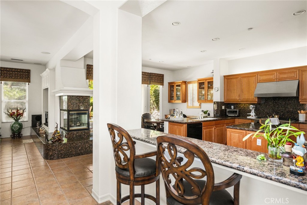 Kitchen with granite breakfast bar, warm wood cabinets, and an adjoining fireplace seating area.
